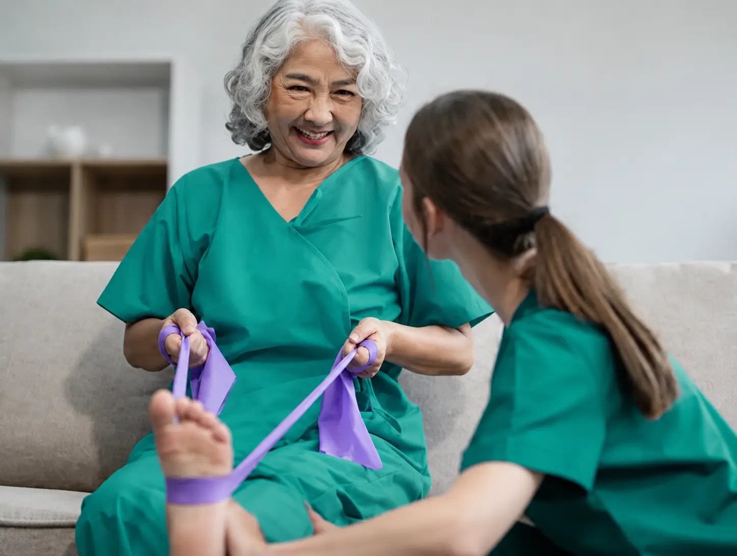 A medical professional providing specialized foot services in Toronto to an elderly woman using a purple resistance band for foot and leg rehabilitation.