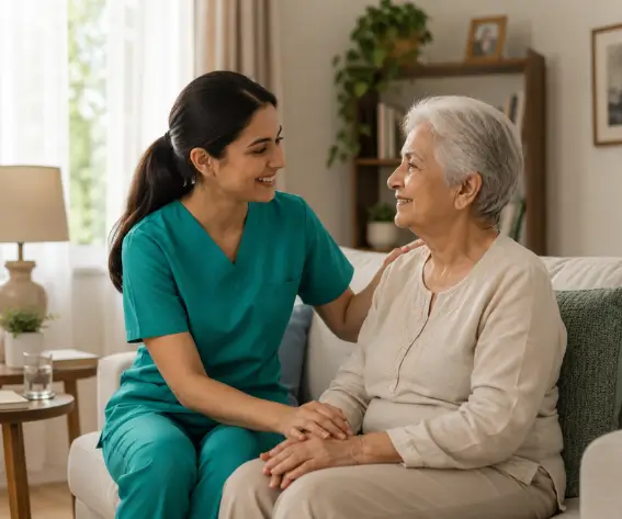 A friendly home care nurse in green scrubs sitting on a sofa and holding hands with an elderly woman, providing professional home care services in Etobicoke.