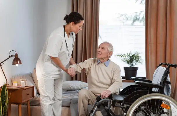 A healthcare professional providing home care in Toronto by assisting an elderly man moving from his bed to a wheelchair.