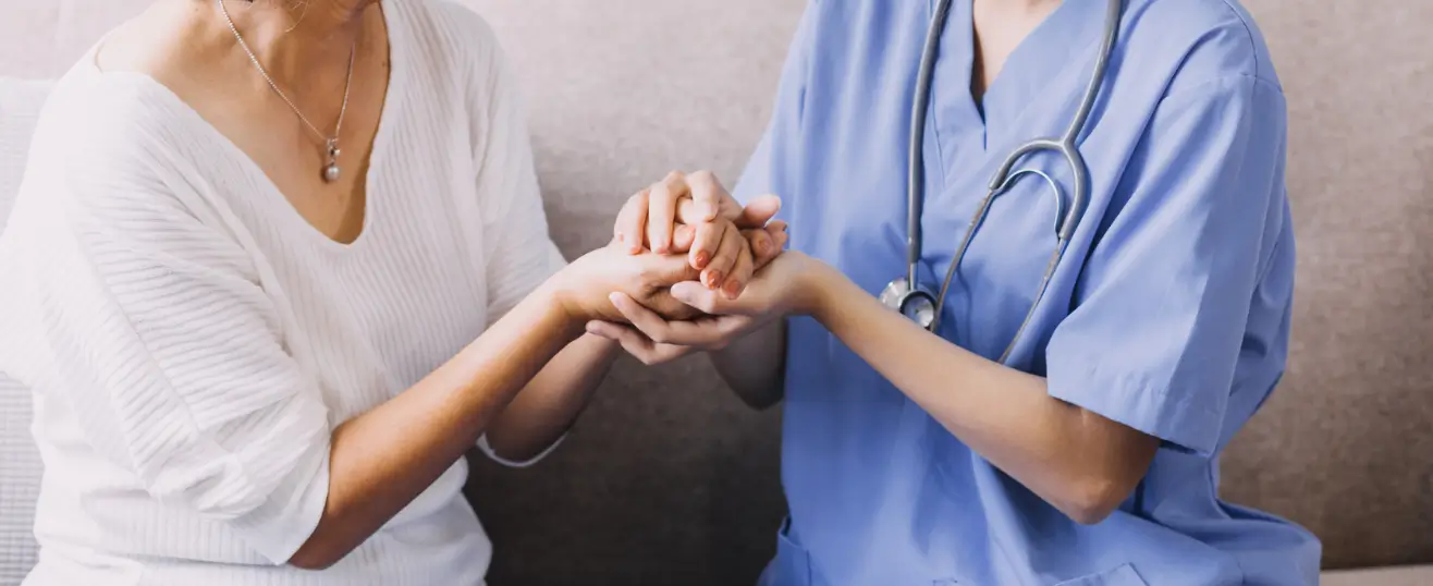 A compassionate nurse in blue scrubs holding an elderly woman's hands during a home visit, illustrating the emotional support and professional nursing services in Toronto available for seniors.