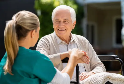 A smiling senior man in a wheelchair holding hands with a supportive caregiver providing compassionate home care in Oakville.