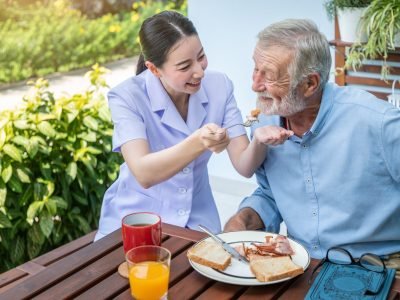 Nurse feeding elderly senior man to eat breakfast at nursing hom